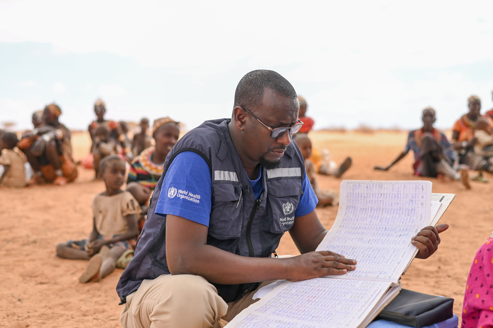<p><sub>2022. szeptember 20-án a WHO munkatársa, Dr. Adam Haji egészségügyi dokumentációkat néz át egy mobil csapat által végzett egészségügyi szűrés során a Marsabitban található Korr faluban. </sub></p>